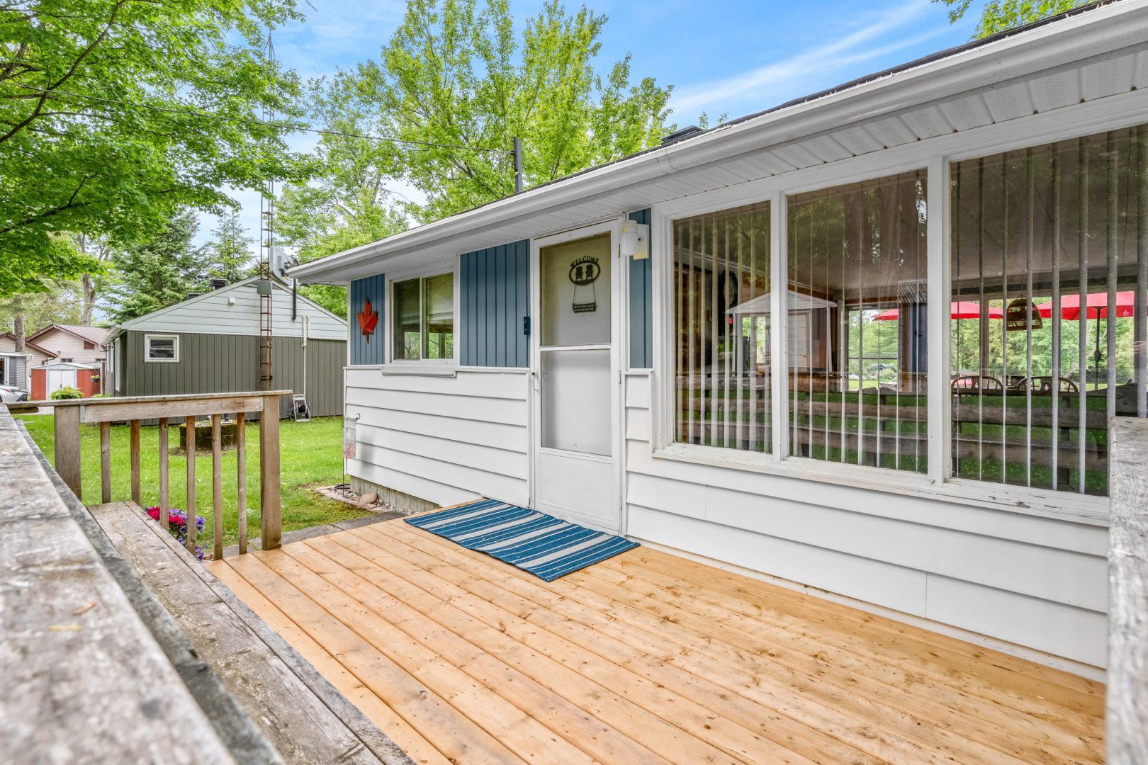 A white clapboard cottage with blue shutters and a light wood deck