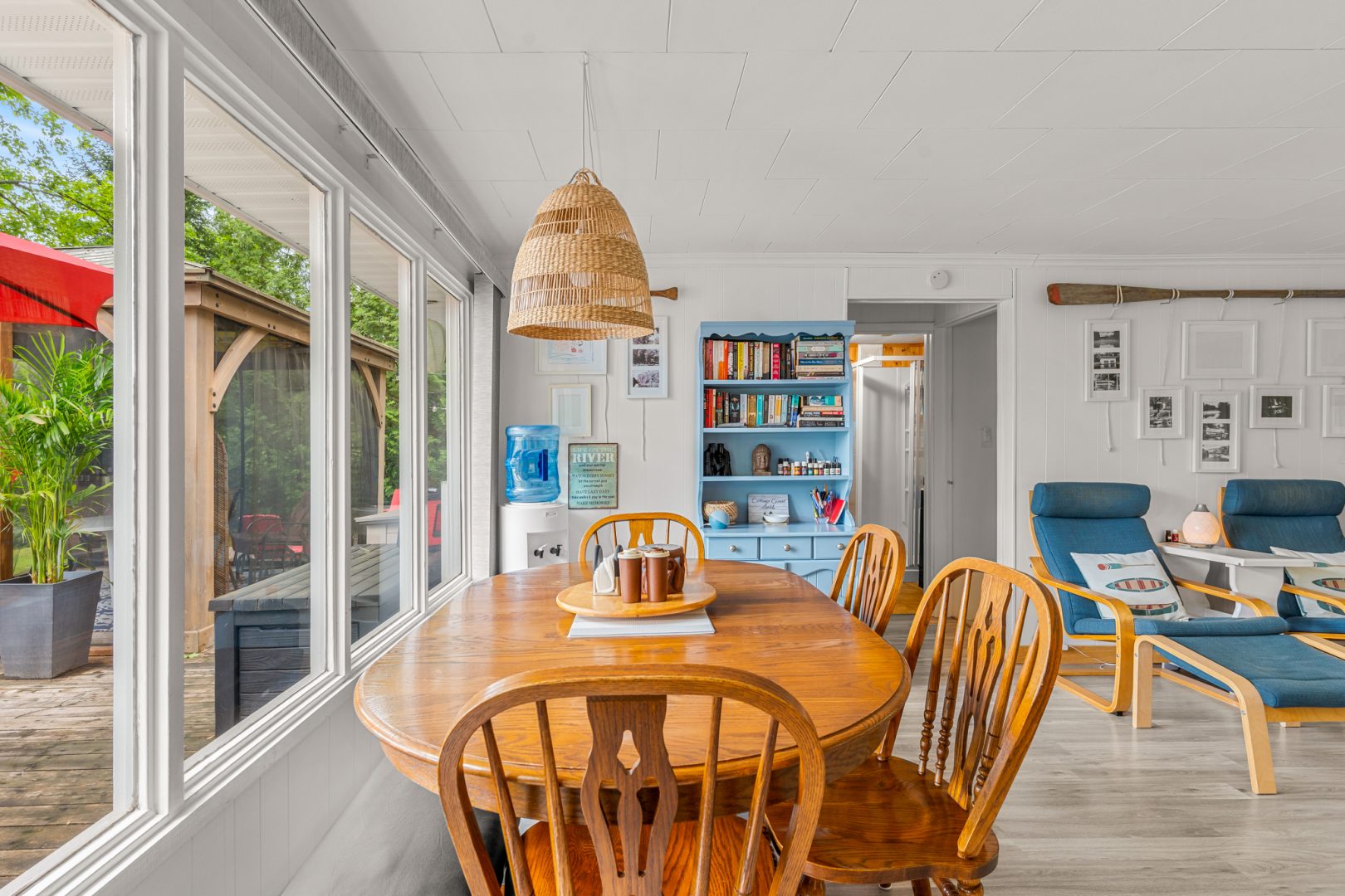 A rounded wood table with wood chairs next to a bright wall of windows