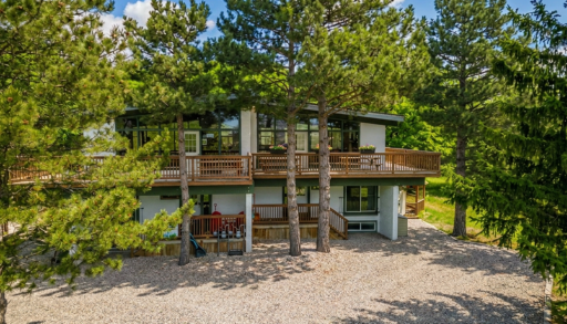 A cottage with a wraparound deck tucked into a forested area