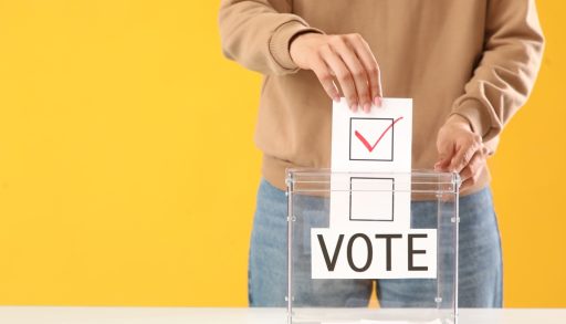 A person putting a ballot into a ballot box on a yellow background