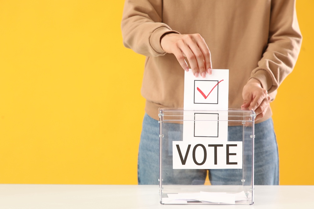 A person putting a ballot into a ballot box on a yellow background