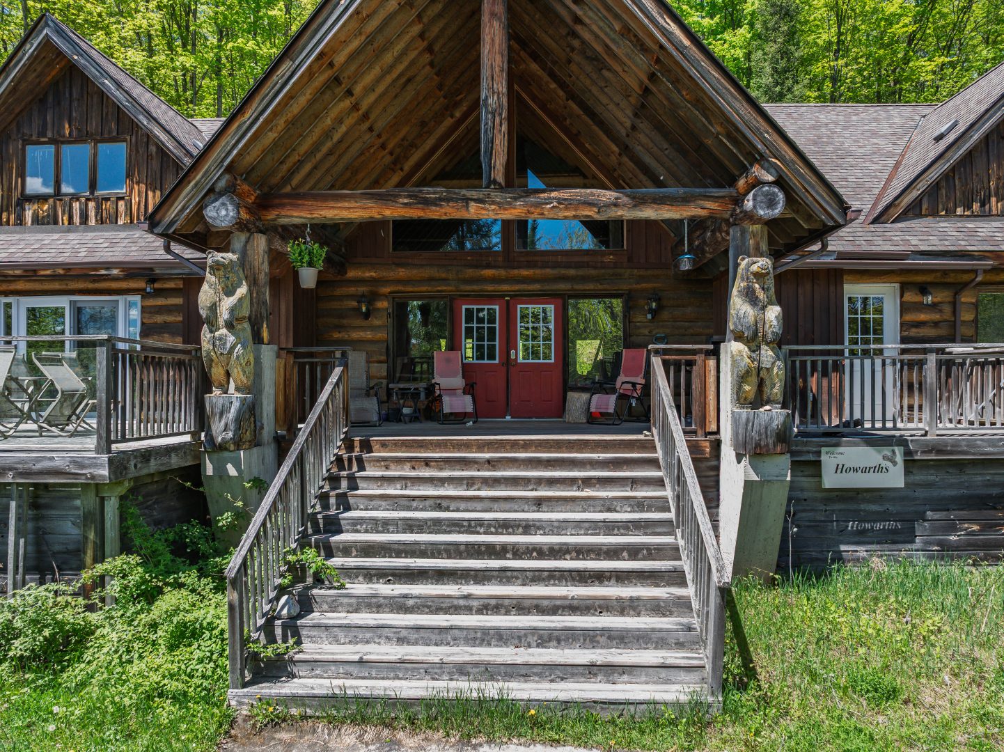 Wood steps lead up to a log cabin with an A-frame front door