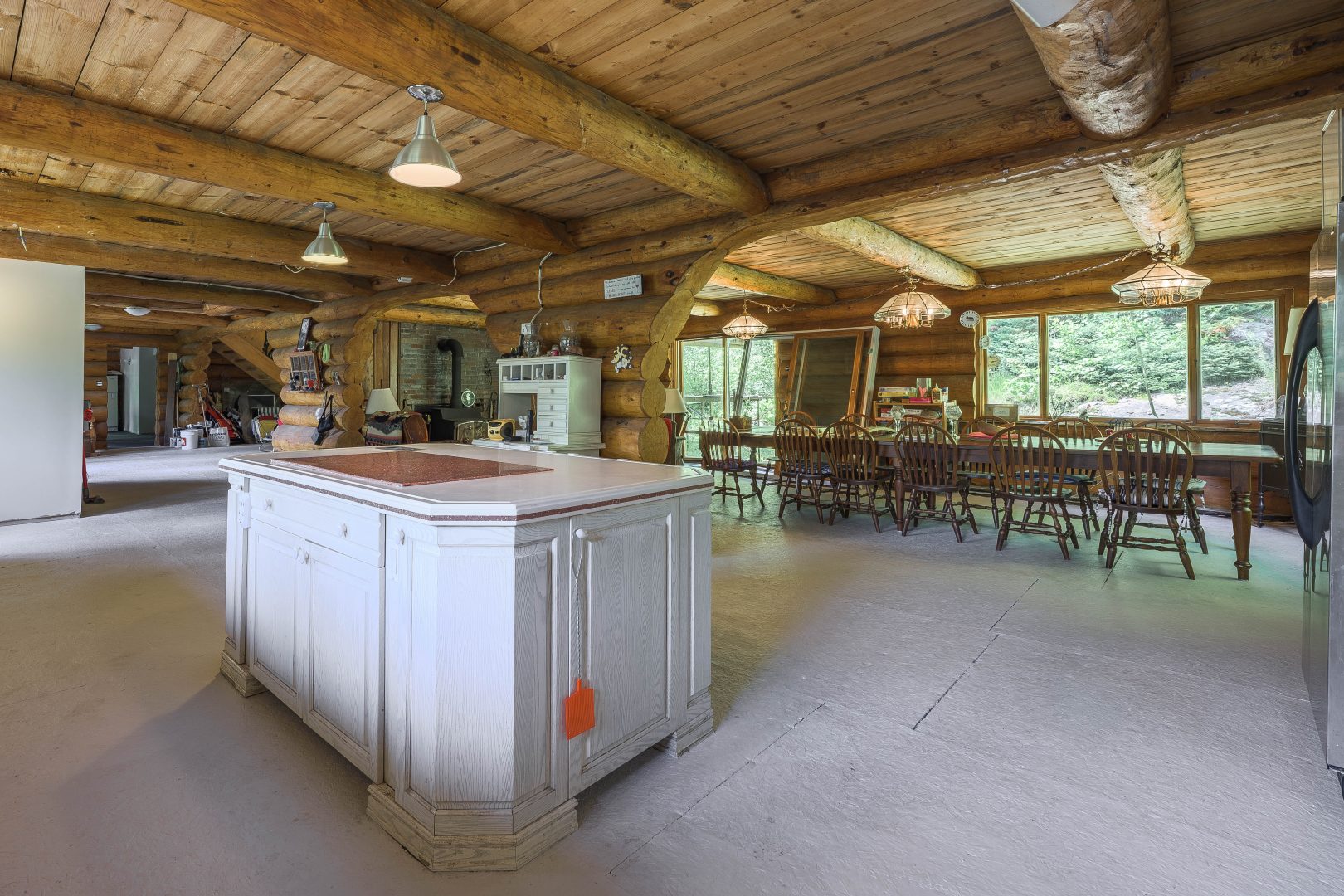 A white kitchen island looks out to a long wood dining table in a wood cabin