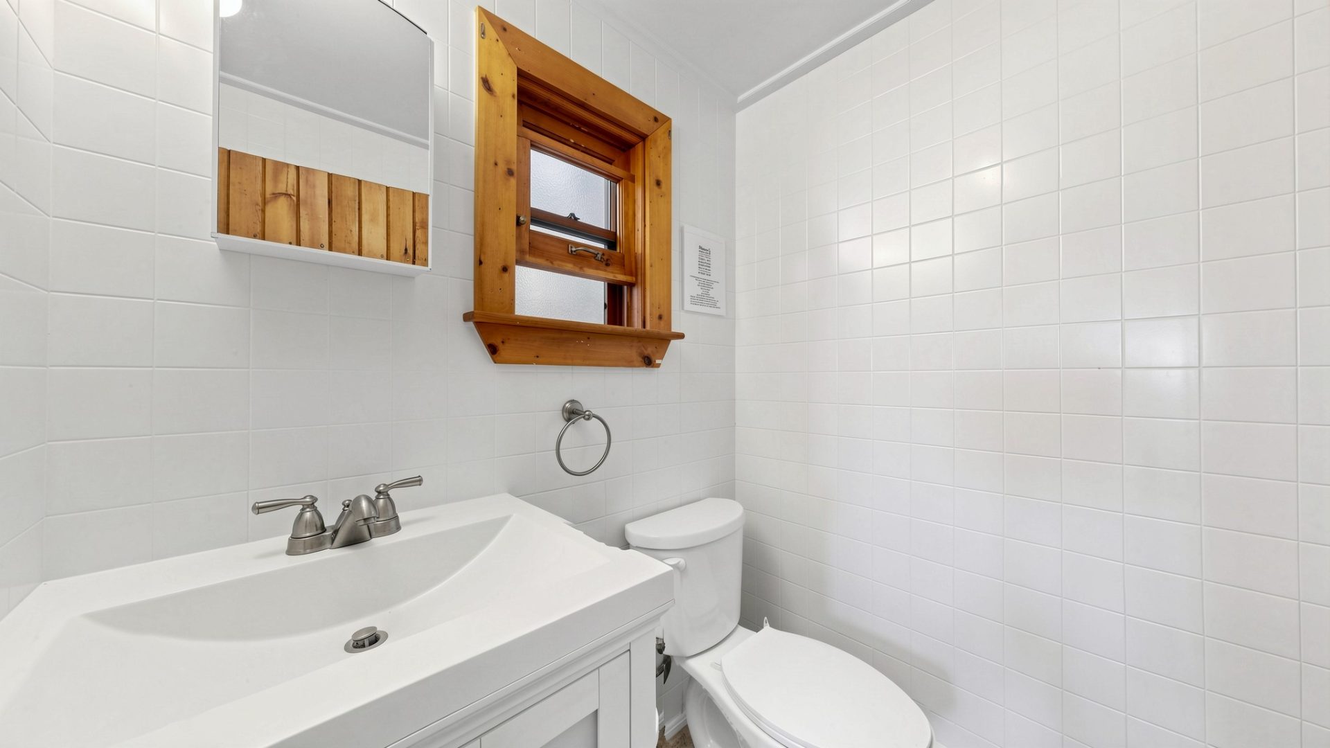 A white bathroom with white appliances and a wood-framed window