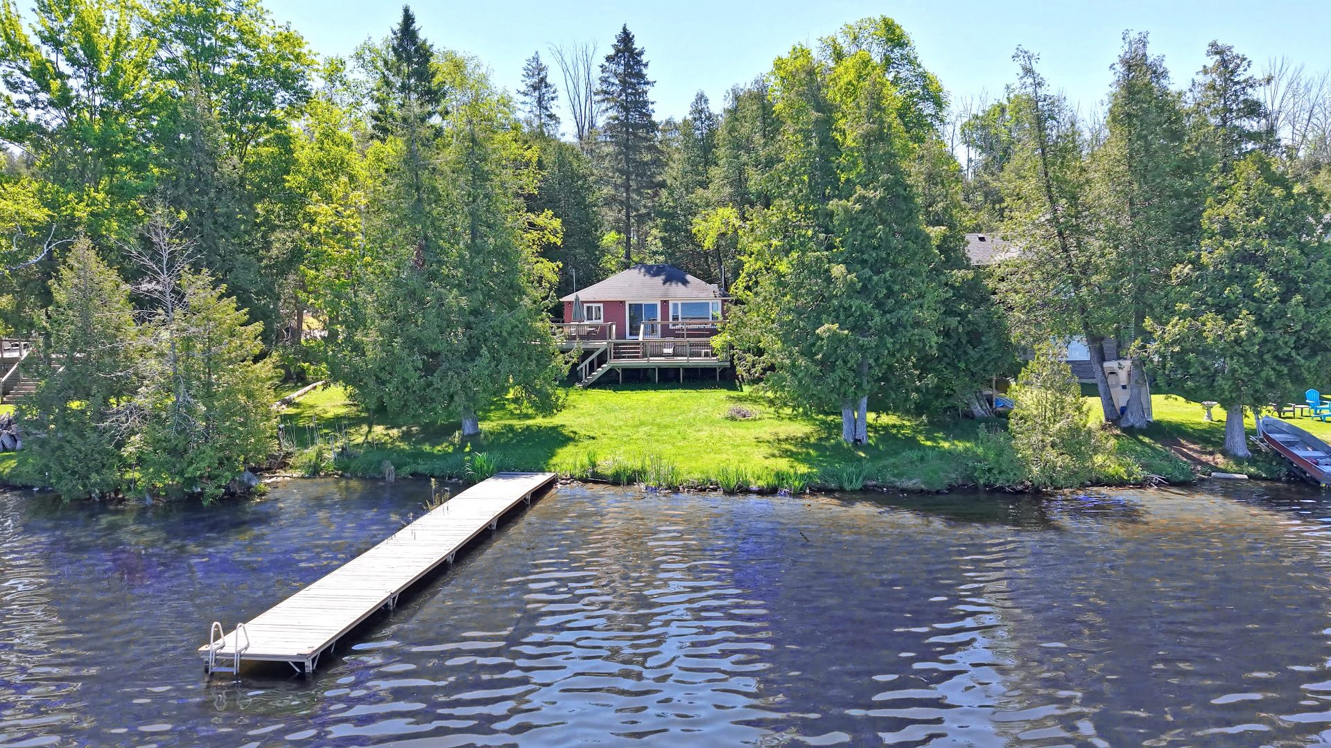 A red clapboard cottage on a grassy property next to the lake