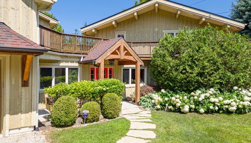 A green clapboard cottage with a red door on a landscaped property