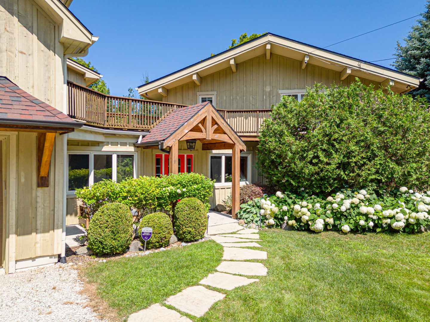 A green clapboard cottage with a red door on a landscaped property