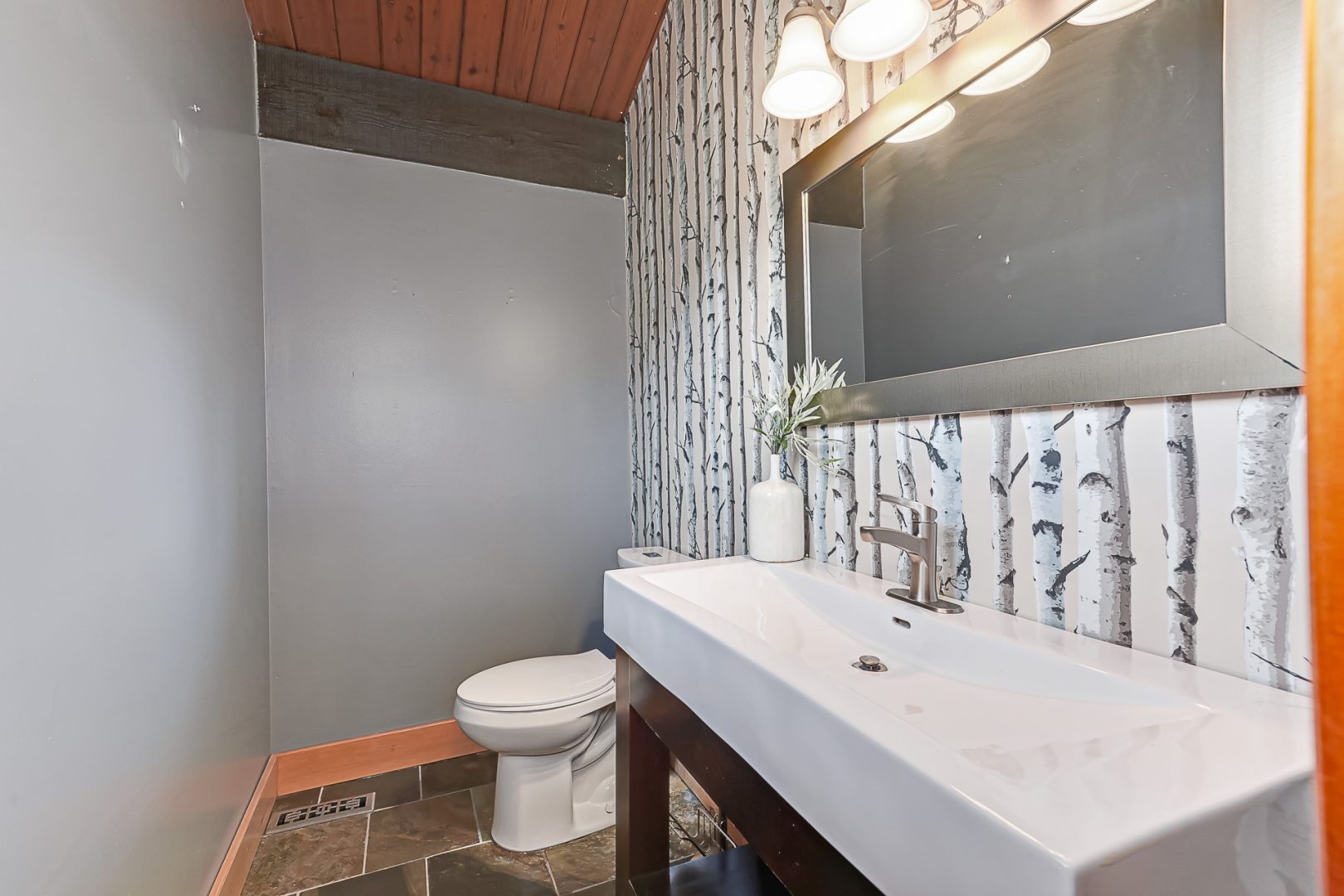 A grey bathroom with birch wallpaper