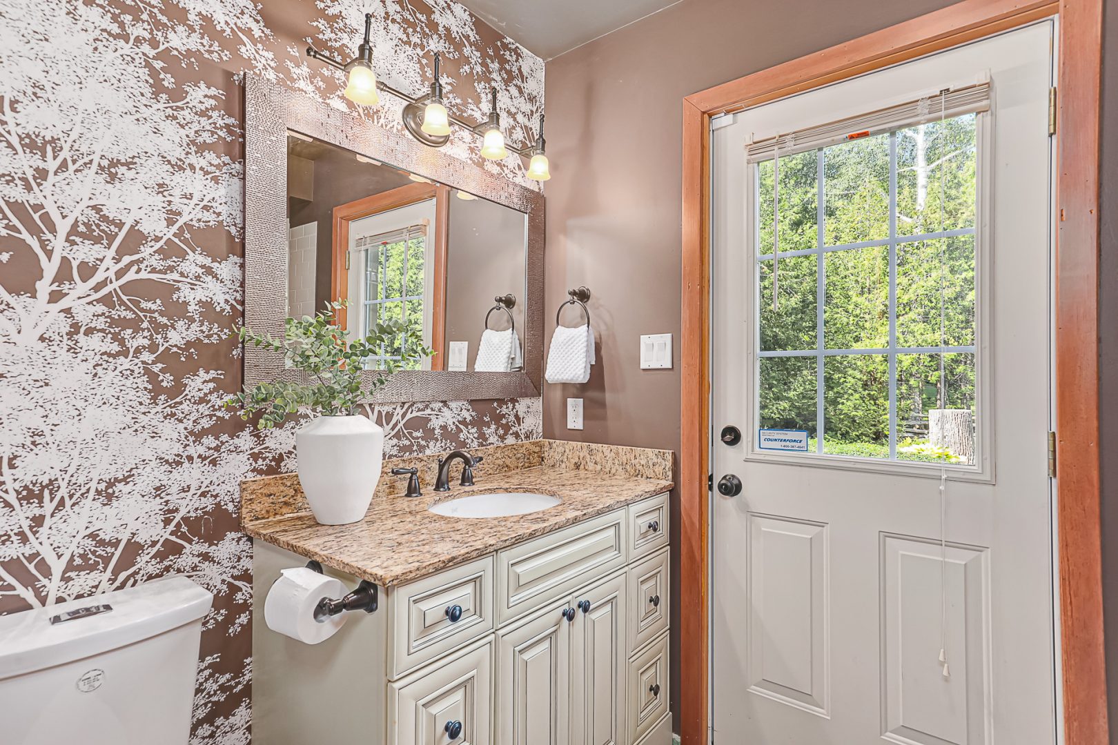 A beige bathroom with patterned wallpaper and a brown vanity