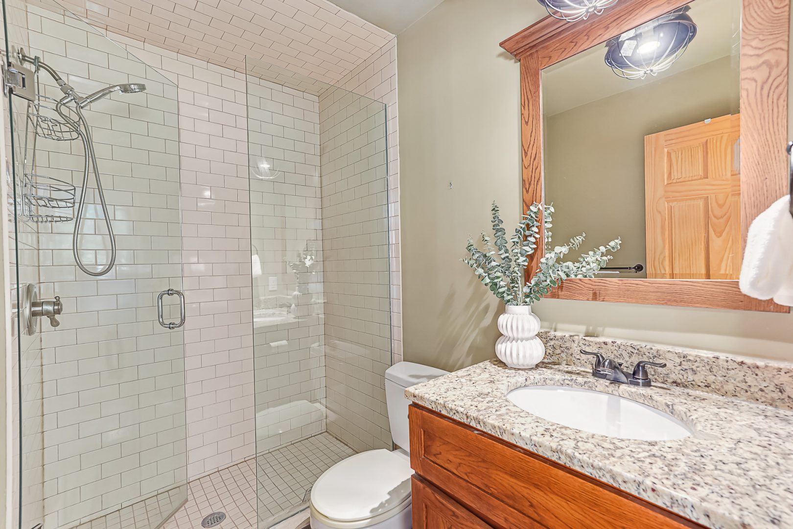 A beige bathroom with a glass walk-in shower and brown vanity