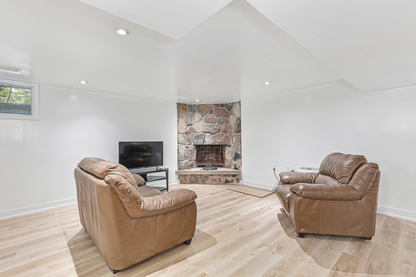 Two light brown sofas face a TV and a stone fireplace in a white room