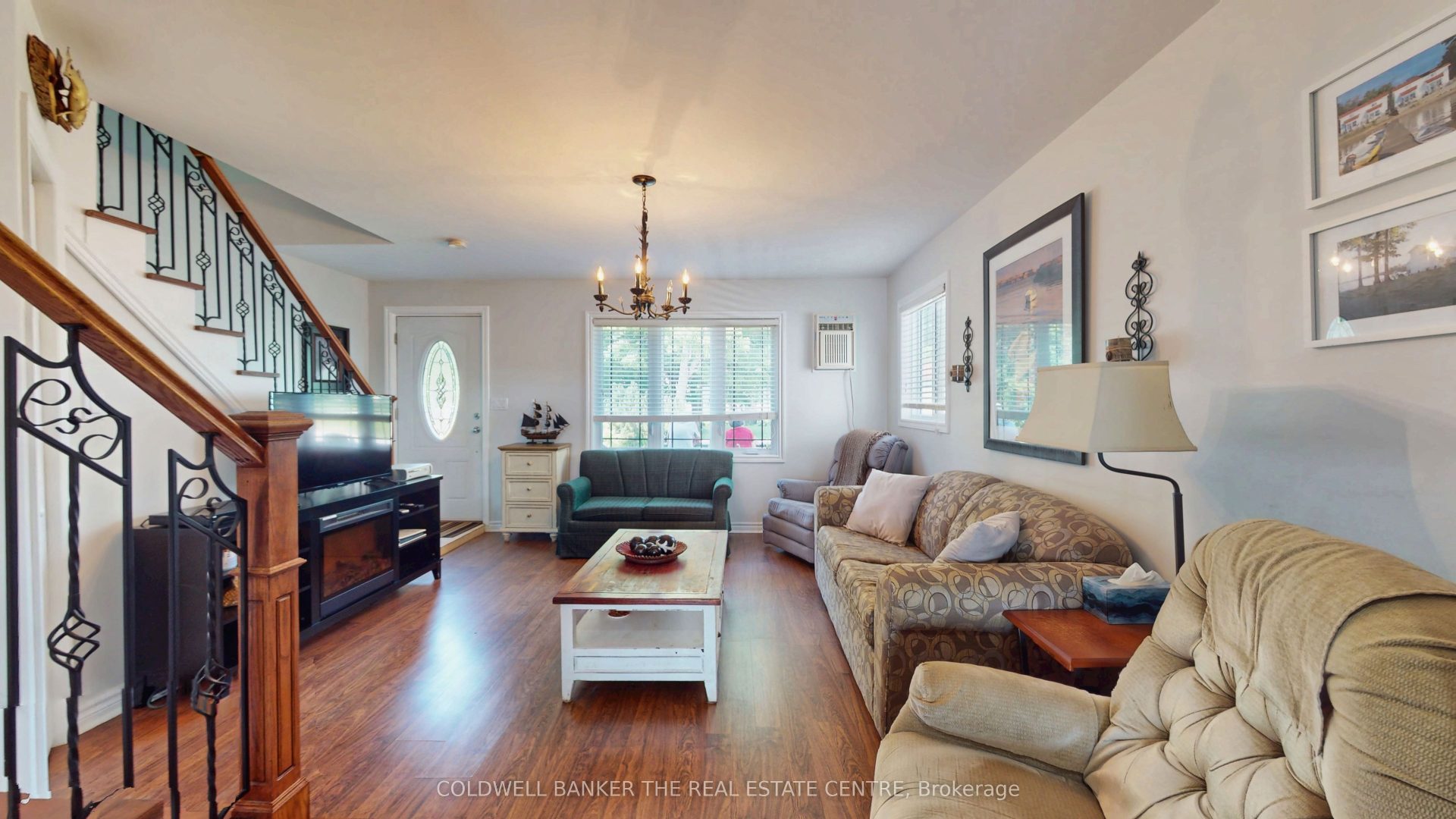 A living room with a patterned brown couch facing a TV stand and staircase