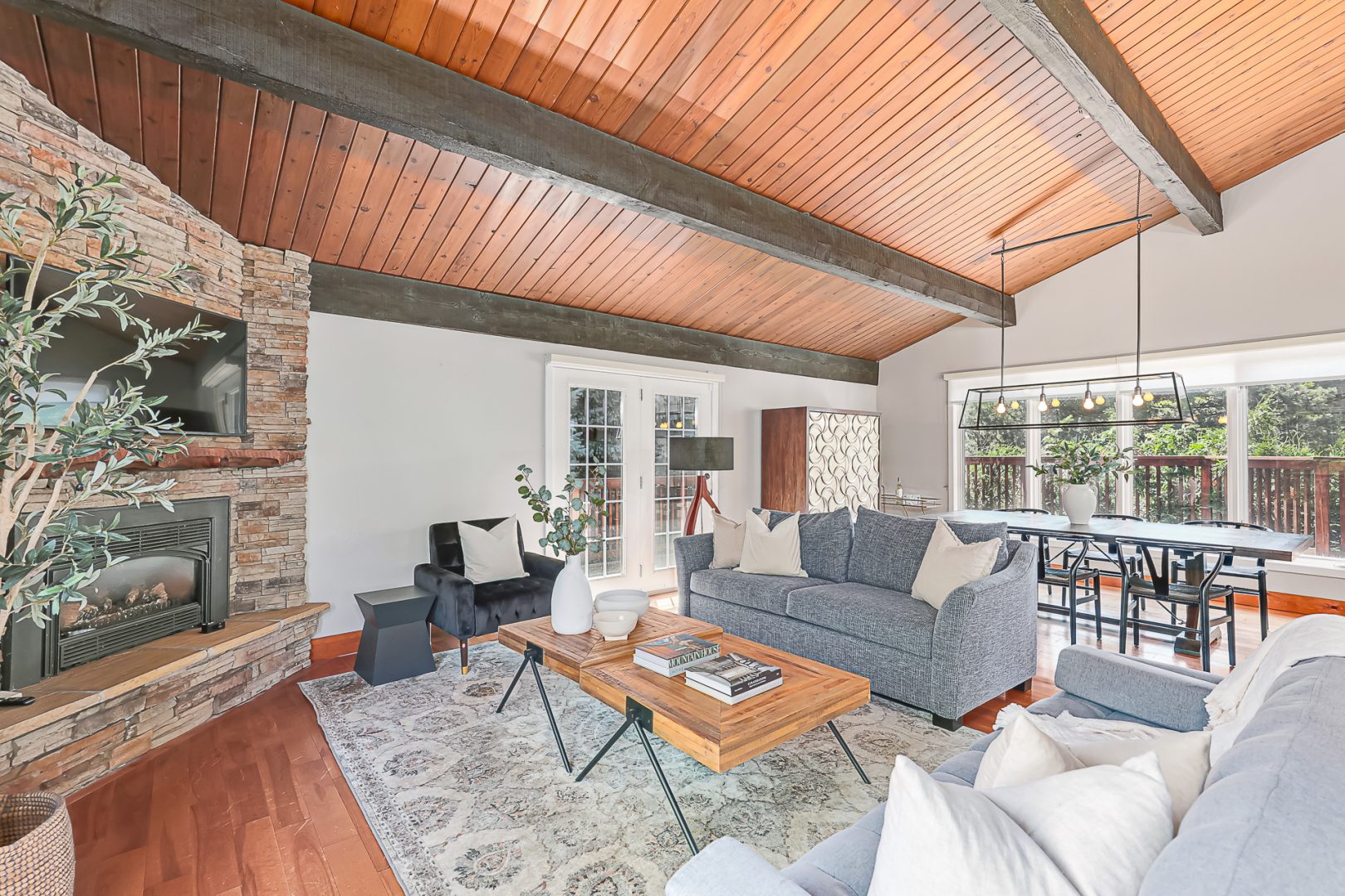 A grey couch facing a light wood coffee table and a stone fireplace in a spacious living room