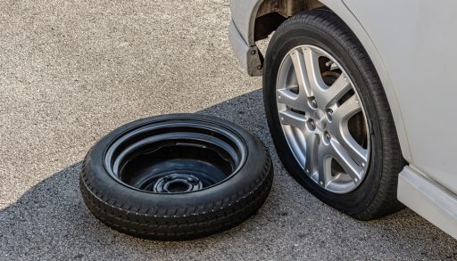 A car with a flat tire and the spare on the ground
