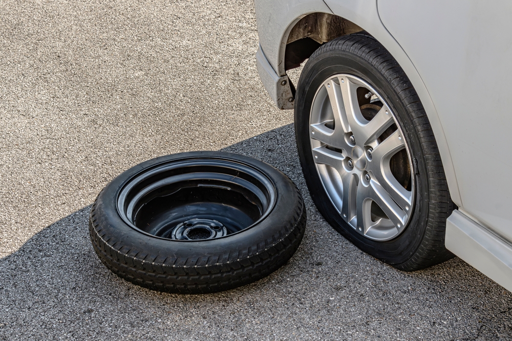 A car with a flat tire and the spare on the ground