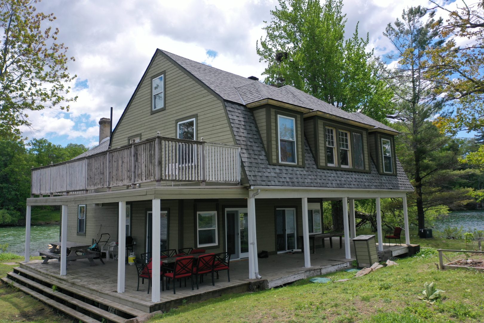 A green-beige clapboard cottage with a balcony