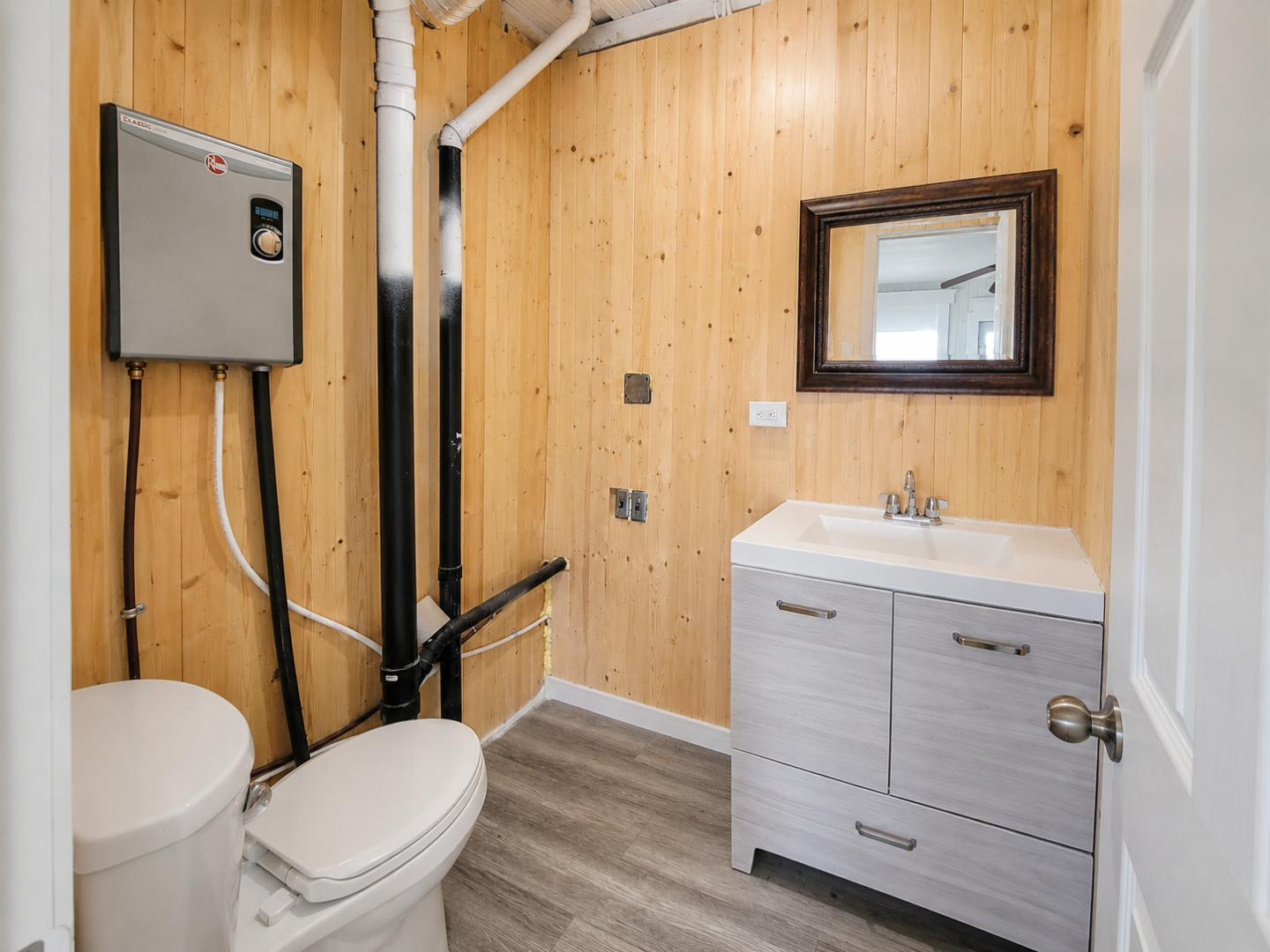 An unfinished paneled bathroom with a white toilet and white vanity