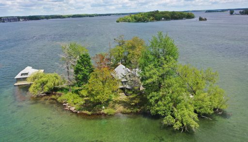 An island with a clapboard cottage surrounded by green-blue water