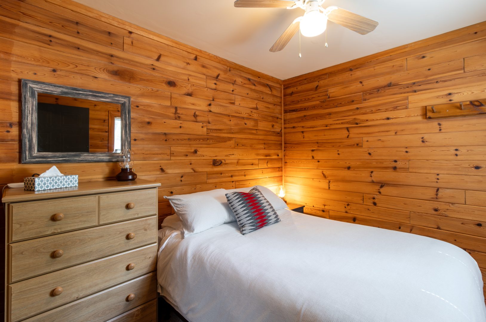 A white bed next to a beige dresser in a wood-paneled room