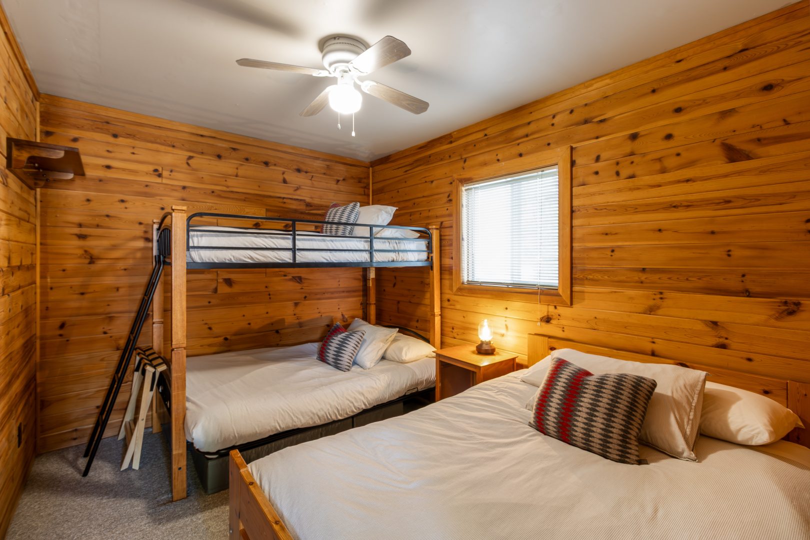 Bunk beds next to a white bed in a wood-paneled room