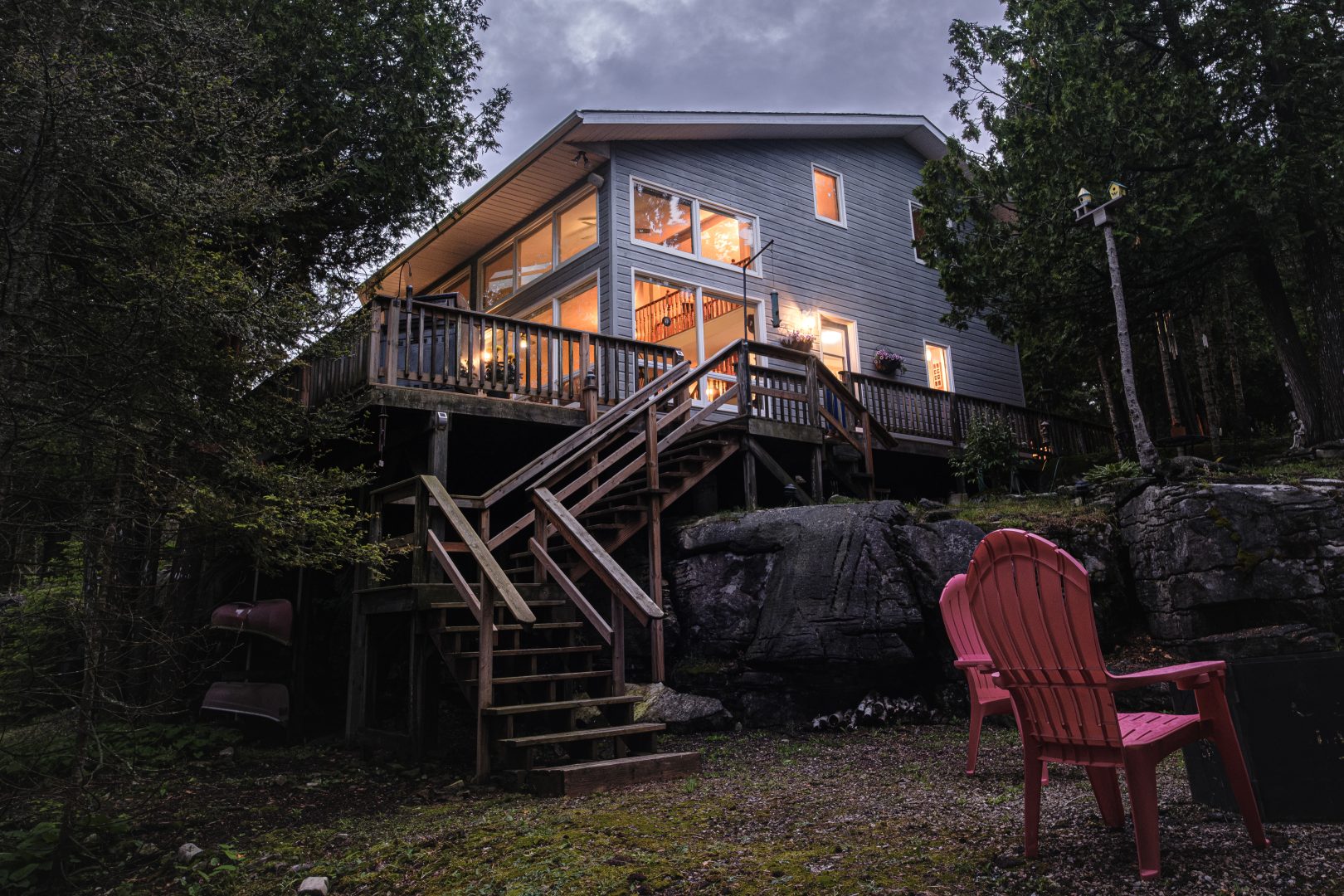 A two-storey cottage with floor-to-ceiling windows is lit up at night