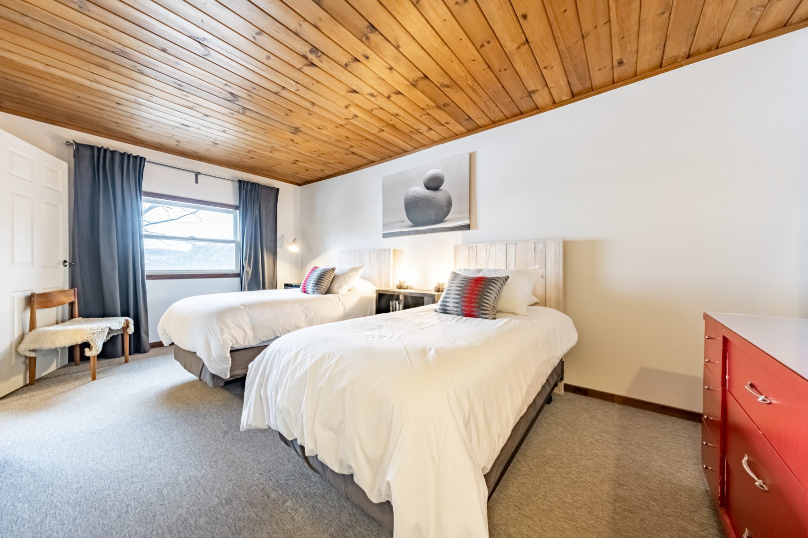 Two white beds in a white bedroom with a wood paneled ceiling