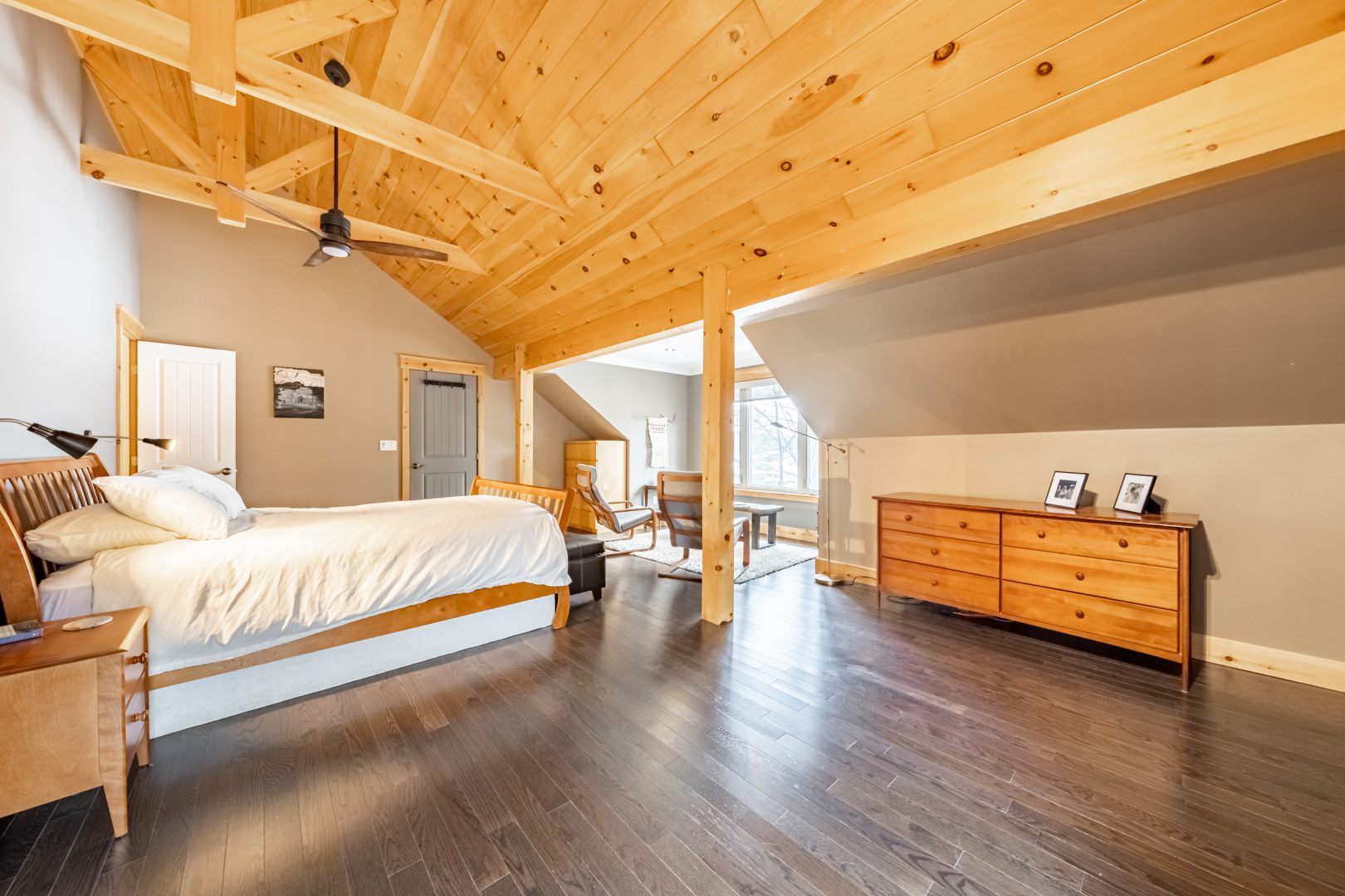 A spacious wood-paneled bedroom with a white bed and vaulted ceilings