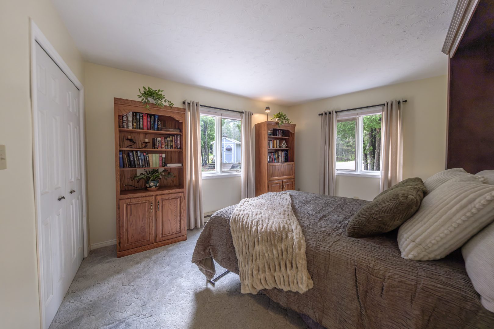 A grey bed in a beige bedroom facing two wood bookshelves
