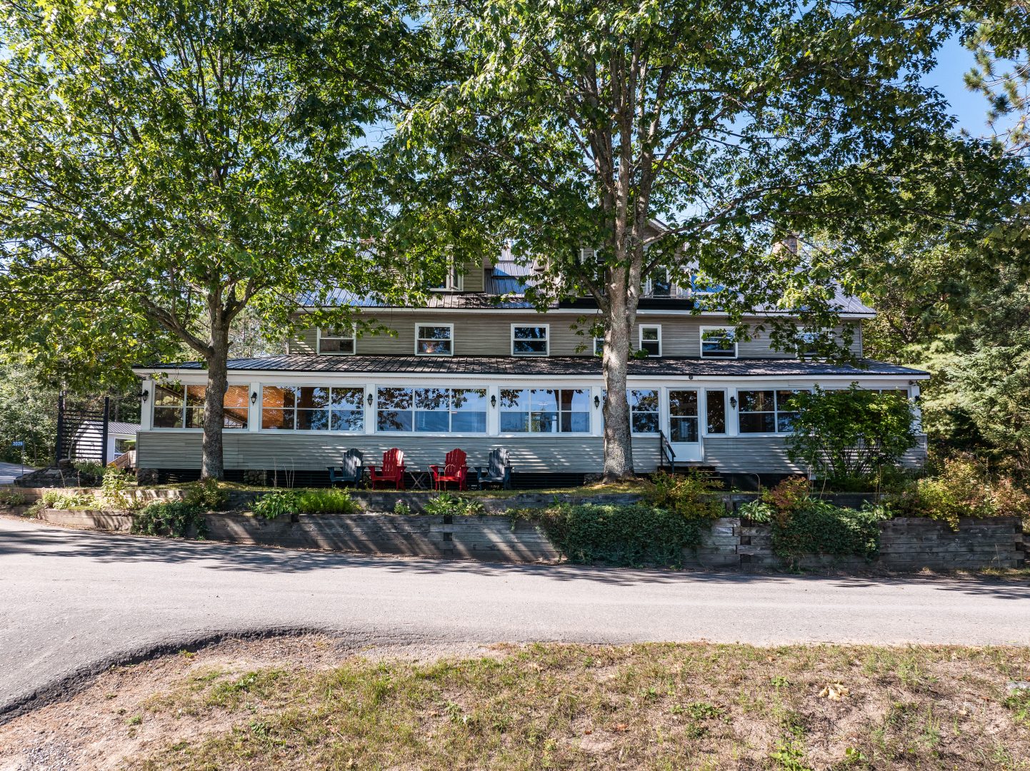 A long clapboard cottage with bright windows and a wraparound porch set back on a tree-lined property