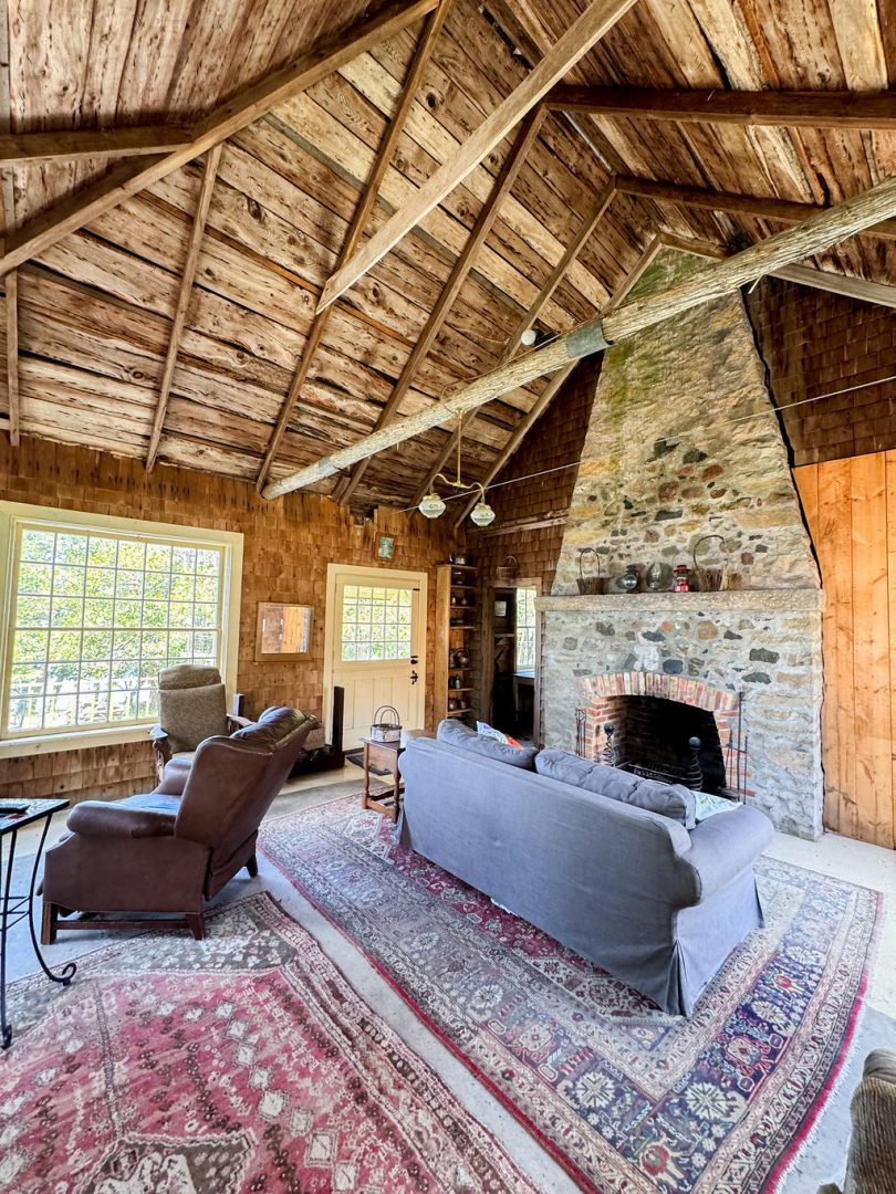 A living room with cathedral ceilings, a patterned red rug, and a grey couch facing a stone fireplace