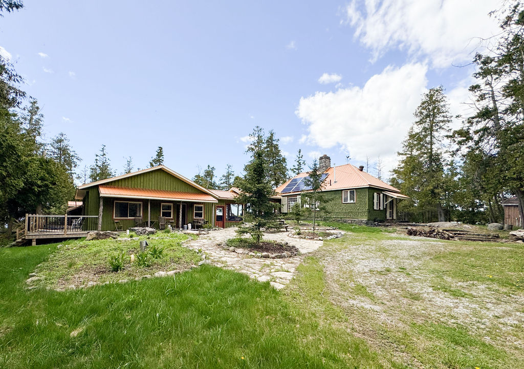 A two-building green cottage dwelling on a grassy property
