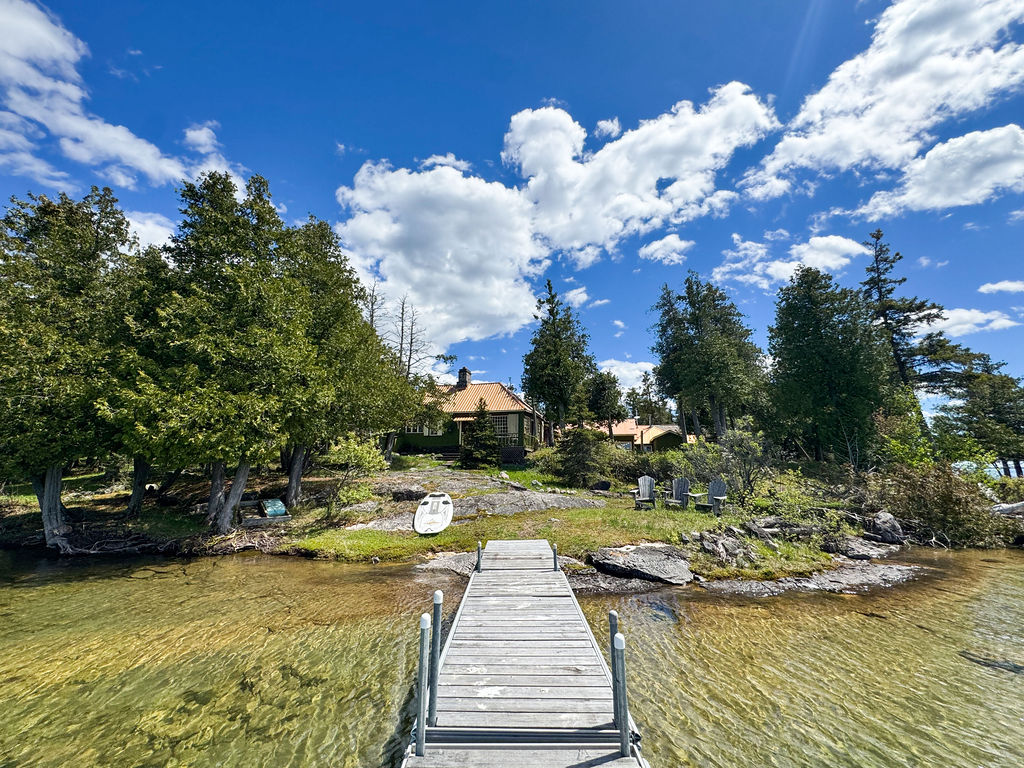 A dock in the water with a green cottage in the background