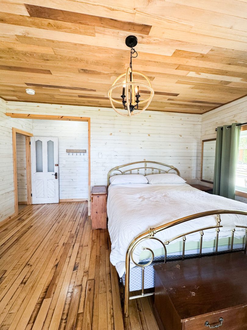 A white bed on a brass bed frame in a wood bedroom
