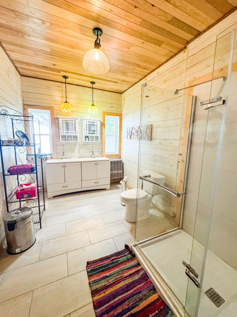 A white bathroom with a glass walk-in shower and a wood ceiling