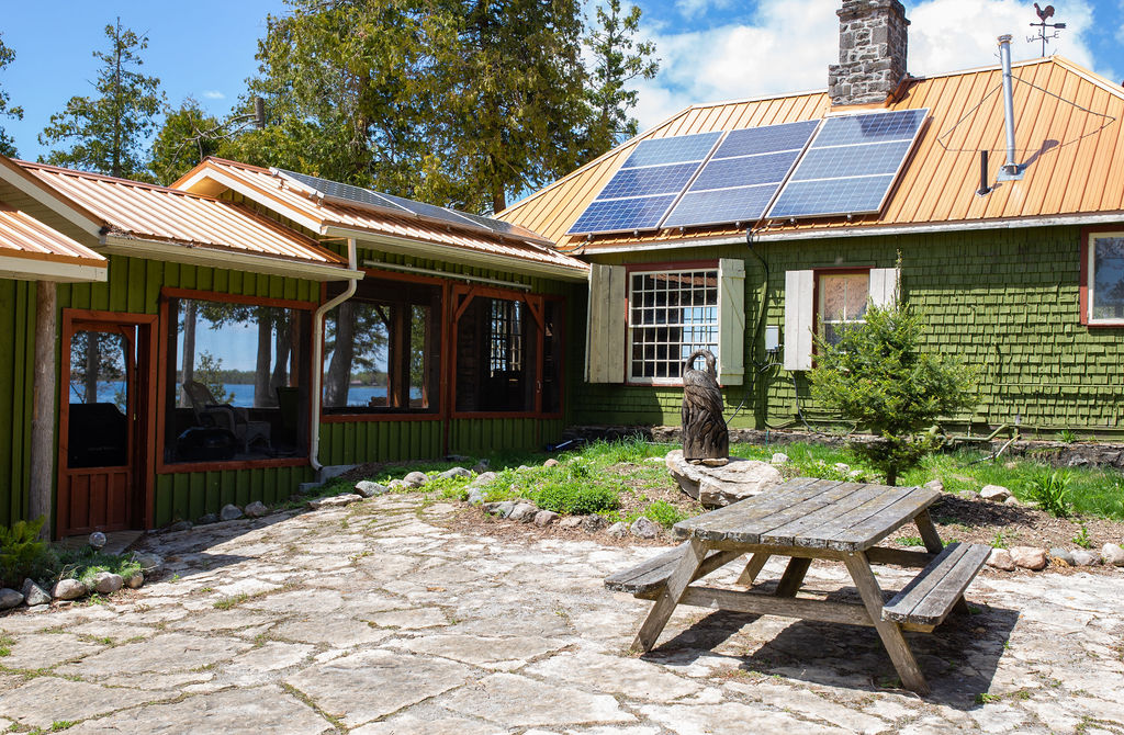 A picnic table on a stone patio next to a green cottage