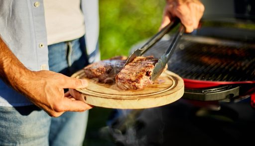 A man placing grilled steaks on a platter