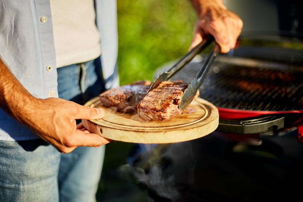 A man placing grilled steaks on a platter