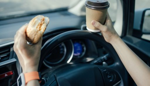 A woman driving while eating a sandwich and drinking coffee