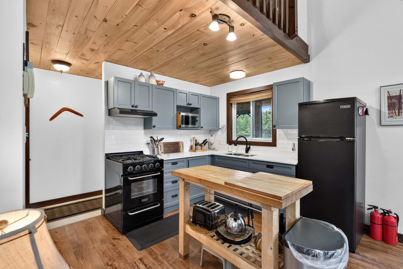 Grey kitchen cabinetry with black appliances and a wood kitchen island