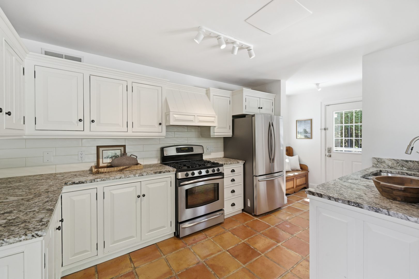 A white kitchen with orange-red hardwood floors with stainless steel appliances