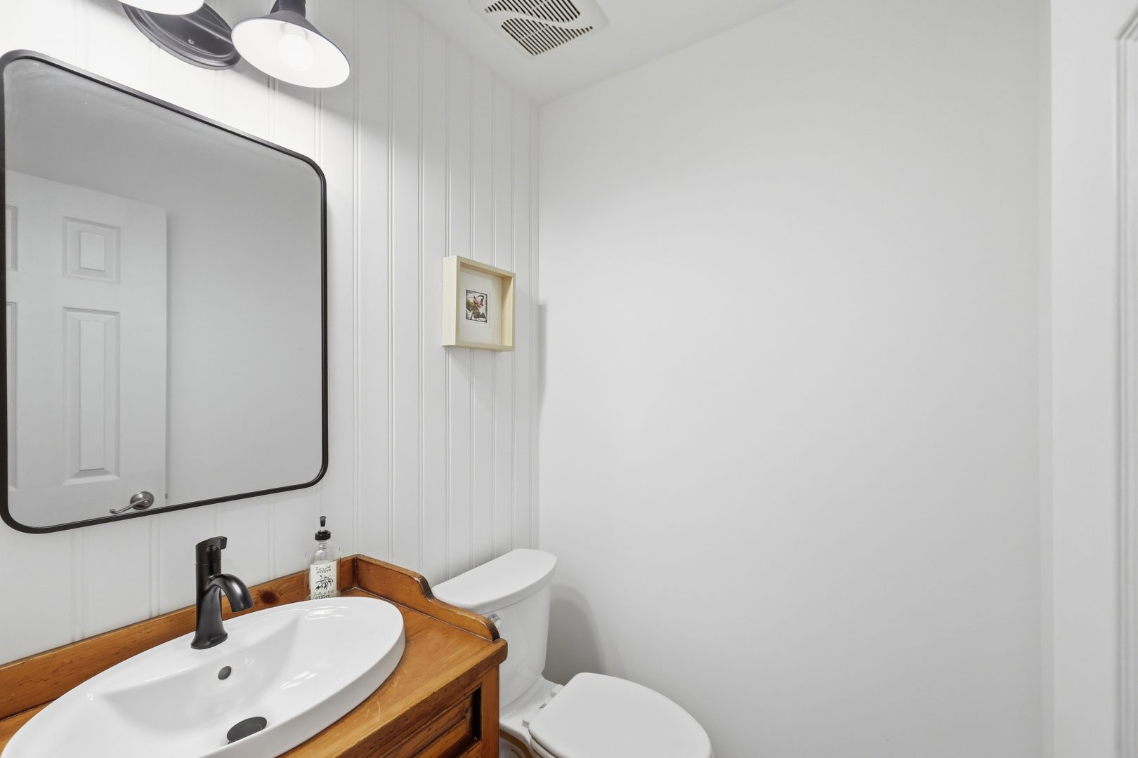 A white bathroom with a wood vanity and a black-framed mirror