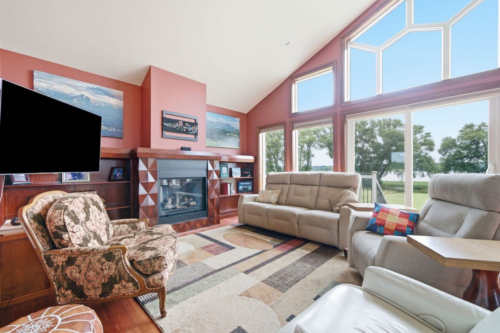 A living room with vaulted ceilings and floor-to-ceiling windows. The walls are a burnt red. Cream couches face each other