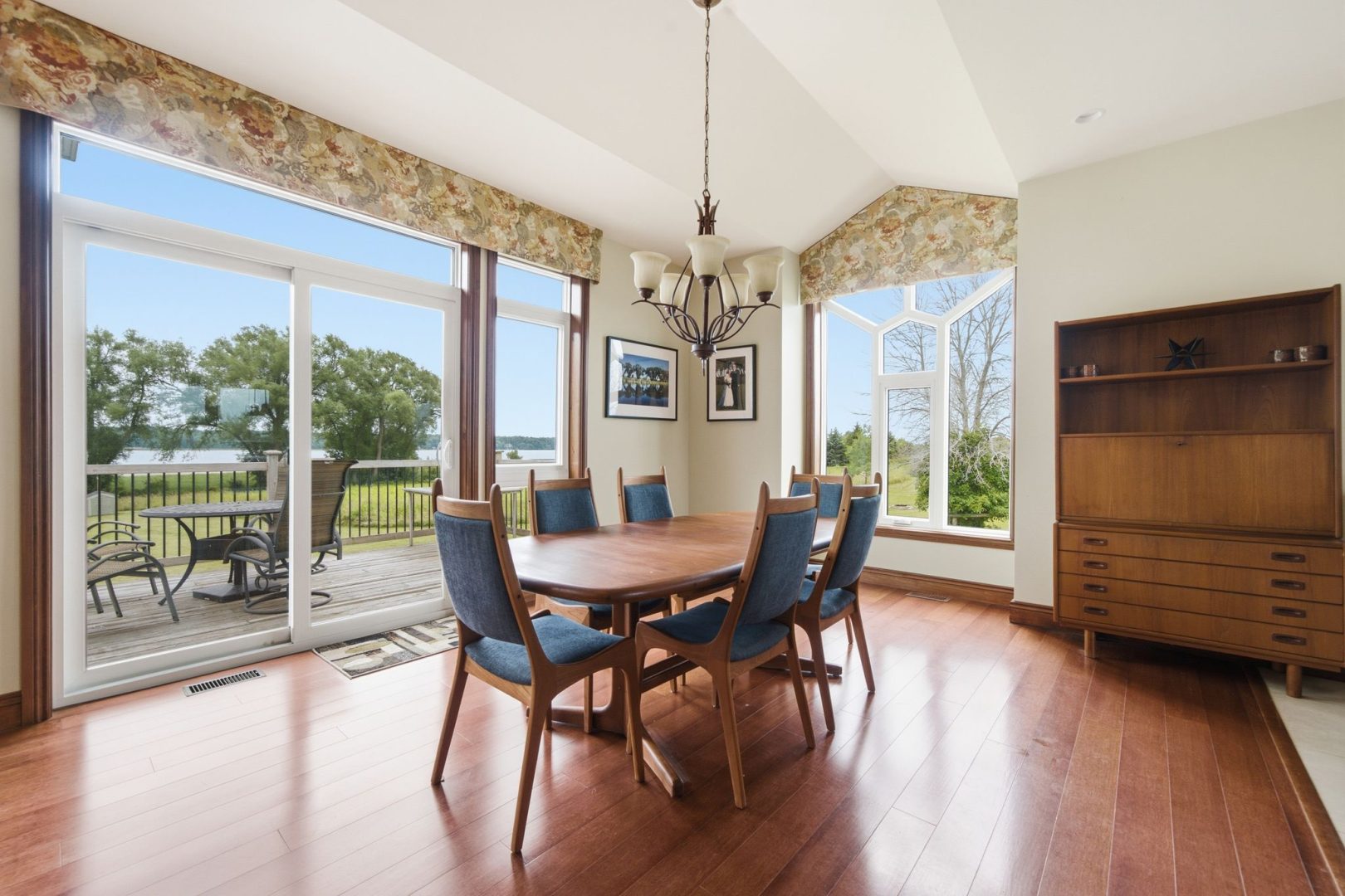 A round wood dining table surrounded by blue upholstered chairs in a sunny dining room