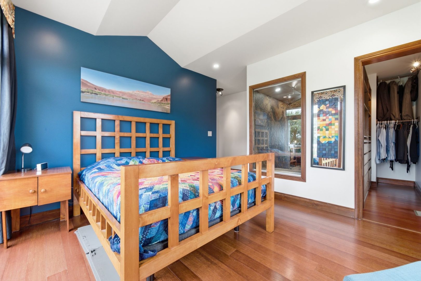 A wood bed frame with a colourful bedspread in a white and blue room